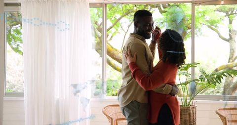 Couple Embracing in Sunlit Sunroom Sharing Smartphone Call with Indoor Plants and Wicker Chairs