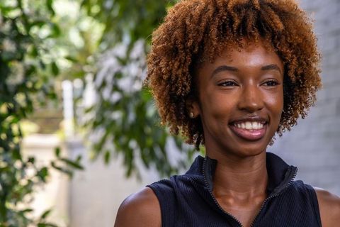 African american woman smiling in garden courtyard with curly hair and casual zip-top