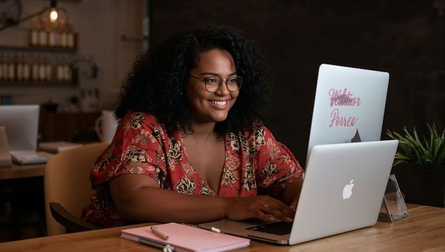Smiling woman working on laptop at cozy cafe table, planning with notebook and coffee