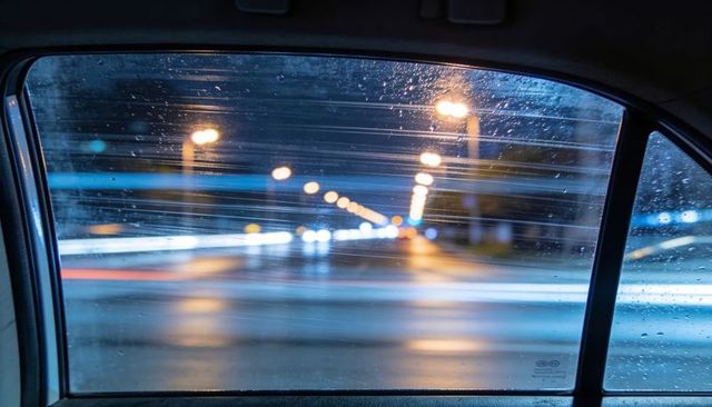 Rain-streaked car window capturing urban light trails and motion blur at night