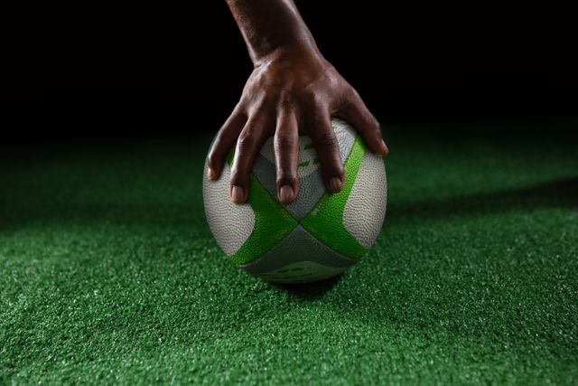 Cropped hand of person on rugby ball against black background