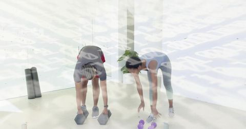 Man and woman bending and reaching dumbbells in bright minimalist gym for partner workout