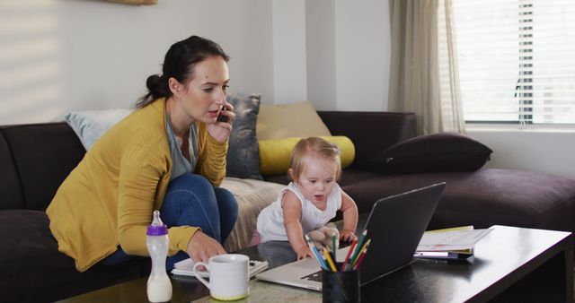 Caucasian mother holding her baby taking notes and talking on smartphone while working from home. motherhood, love and childcare concept