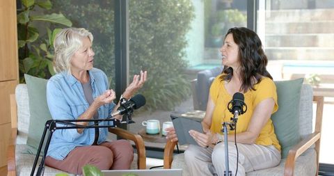 Two women recording podcast conversation in bright home living room