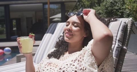 Relaxing african american woman lounging by pool with cocktail sunglasses crochet coverup