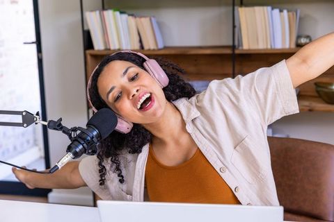 African american woman energetically hosting podcast in home studio wearing pink headphones