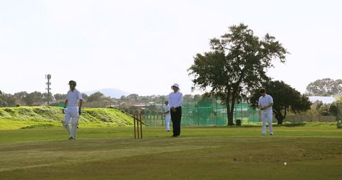 Cricket Players and Umpire on Sunny Field Holding Ball Beside Stumps