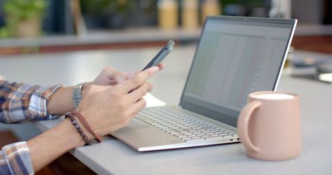 Young Professional Multitasking with Smartphone and Laptop in Modern Office
