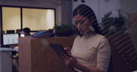 Female professional using tablet in dim open-plan office working late