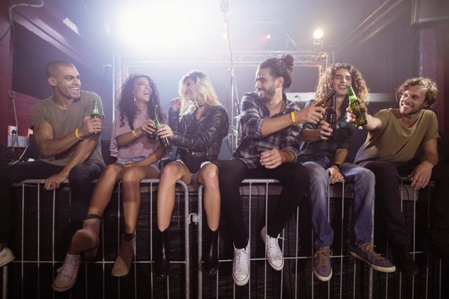 Group of friends enjoying a night out at a nightclub, toasting with beer bottles. Perfect for use in advertisements for nightlife venues, social events, beverage promotions, or articles about young adult social life and entertainment.
