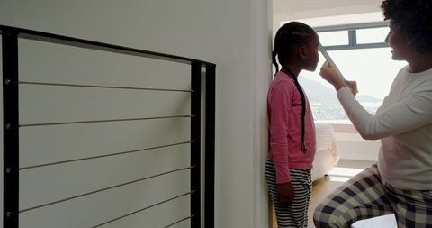 Mother Measuring Daughter's Height at Home Near Bright Window