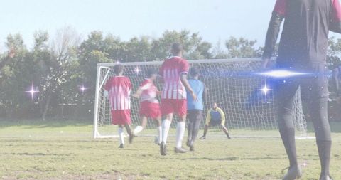 Male soccer players attacking goal during outdoor match with lens flare, teamwork, competition