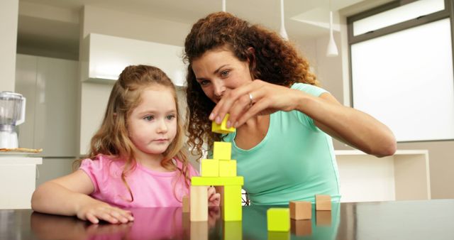 Mother and daughter playing with building blocks at the table at home in kitchen