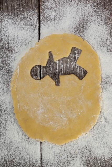 Gingerbread dough with a cut-out shape on a floured wooden surface. Ideal for holiday baking themes, recipe blogs, festive advertisements, and kitchen decor.
