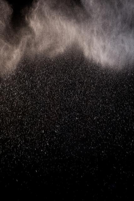 Close-up dust particles floating in air against a black background creating a dramatic mist effect. Can be used in various creative projects such as backgrounds, design elements, or illustrating concepts like pollution, cleanliness, or environment.