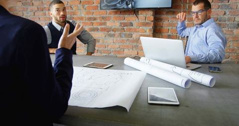 Reviewing blueprints and digital plans: team collaborating industrial brick conference room