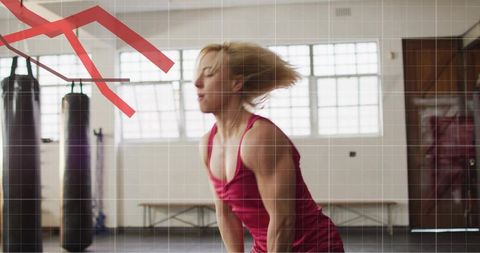 Female athlete jumping during hiit training in gym with punching bags and red overlay