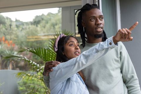 Black man and south asian woman exploring new home pointing toward garden through sliding door