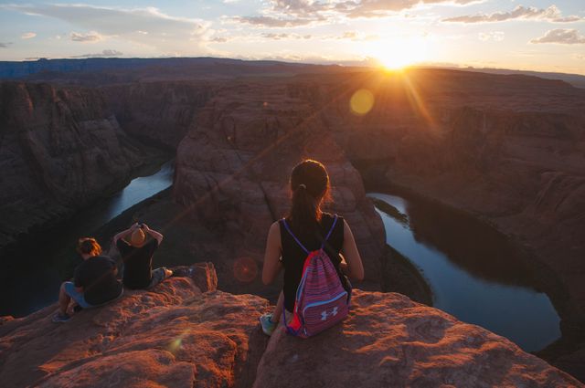 People sitting on rocks and enjoying breathtaking view of Horseshoe Bend during sunset. Perfect for use in travel brochures, adventure blogs, environmental awareness campaigns, and social media posts promoting outdoor activities and nature exploration.
