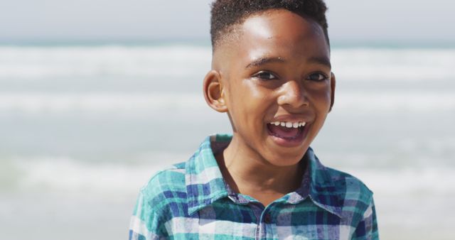 Young boy wearing checkered shirt experiencing joy by the ocean. Great for use in advertising family vacations, summer activities, outdoor fun, joy, and childhood happiness.