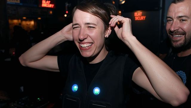 Laughing woman adjusting hair wearing led vest at vibrant nightclub dj party