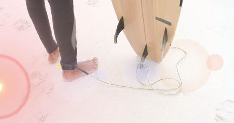 Surfer holding board on sandy beach with light flares