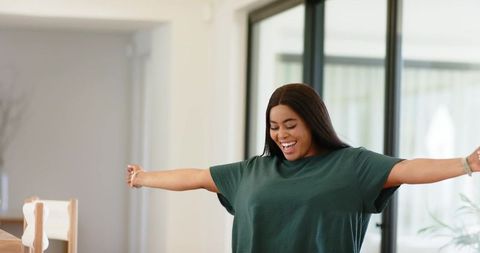 African american woman stretching arms joyfully in sunlit minimalist home interior
