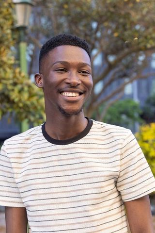 African american man smiling in urban plaza wearing striped tee, friendly outdoor portrait