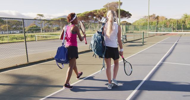 Image of back of diverse female tennis players holding racket, walking and talking. professional tennis training, sport and competition concept.