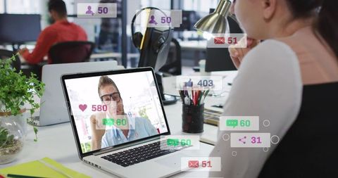 Woman holding mug watching virtual meeting with social reactions overlay in modern office