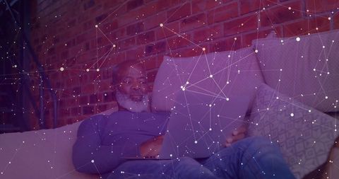 Senior Man Relaxing on Sofa with Laptop in Modern Loft