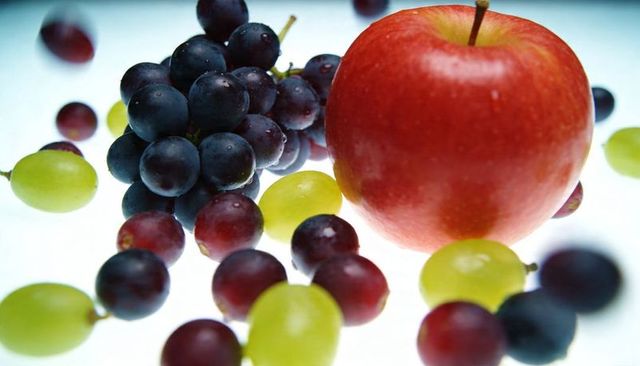 Red apple with green and purple grapes and water droplets on bright high-key studio surface