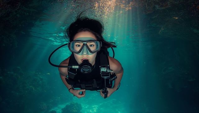 Solo female scuba diver exploring vibrant coral reef under sunbeams in turquoise ocean