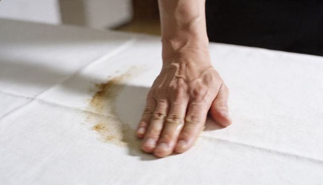 Right hand pressing on stained white tablecloth closeup for cleaning and stain removal