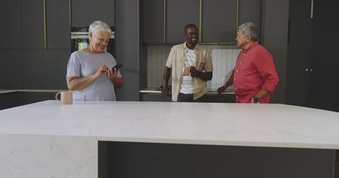 Multigenerational family chatting at marble kitchen island, senior woman tapping phone