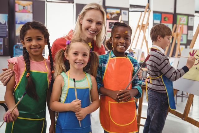 Image showing an art teacher with diverse school children in a cheerful drawing class. The students are wearing colorful aprons and holding paint brushes. This image can be used for educational materials, school brochures, advertisements for art supplies, or articles about creative learning environments.