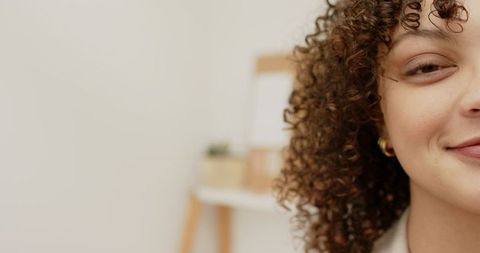 Smiling professional woman posing with curly hair and gold hoop earring in neutral studio