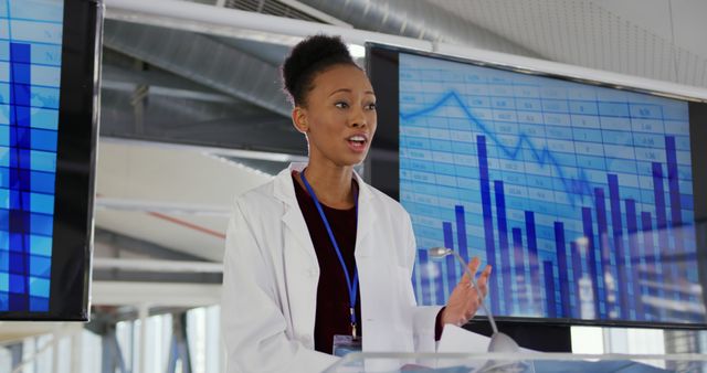 African American female scientist giving a presentation with data charts in background. Useful for topics related to scientific research, healthcare, professional women, and technology presentations.