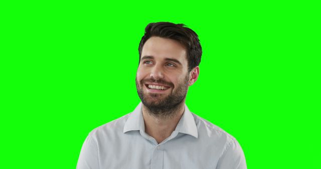 Young man with a beard wearing a white shirt smiling and looking off to the side against a green screen background. This photo can be used for visual effects, marketing materials, advertisements, or presentations to show a happy and content individual. Ideal for use in promotional content suggesting positivity, friendliness, and happiness.