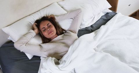 Relaxed Woman Stretching on Comfortable Bed in Minimalist Bedroom