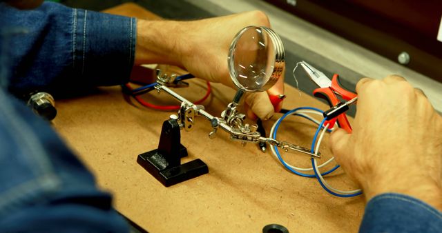 Close-up of technician performing electronics repair using magnifying glass and various tools on a circuit board. Useful for illustrating concepts related to technology, engineering, repair services, and hands-on work in a workshop.