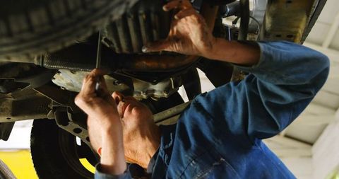 Mechanic inspecting car undercarriage while repairing oil pan with wrench on lift