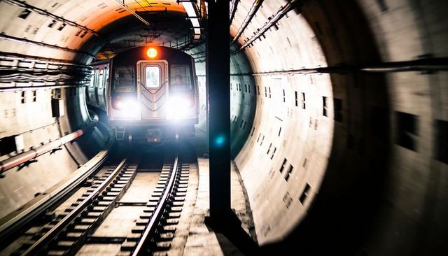 Approaching subway train in curved concrete tunnel with bright headlights and twin rails