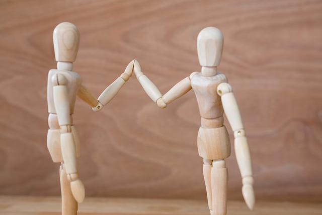 Wooden art mannequins holding hands, symbolizing friendship, teamwork, and unity. Ideal for illustrating concepts of partnership, collaboration, and support in creative projects, educational materials, and motivational content.
