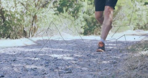 Male trail running legs midstep on rocky gravel path with orange shoes and sunlit forest