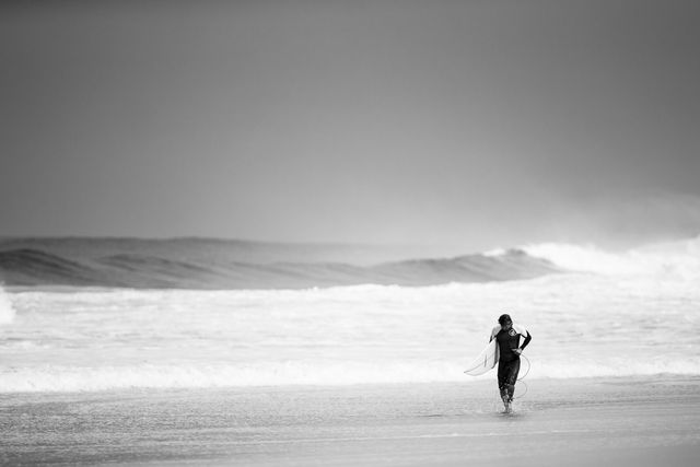 Capturing a moment of tranquility as a lone woman strolls along a calm beach by the ocean. This monochrome photo emphasizes solitude and peacefulness. Perfect for projects related to mental health, relaxation, travel, or even artistic expressions focusing on serene moments.