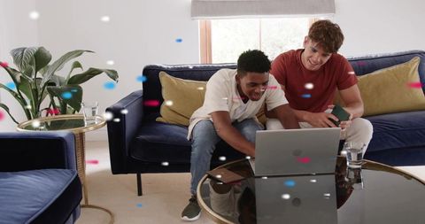 Friends celebrating online win while using laptop on modern living room sofa with confetti
