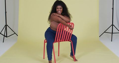 Confident Woman Embracing Bold Chair Against Yellow Studio Background