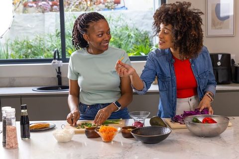 African American Friends Chopping and Tasting Vegetables at Modern Kitchen Island