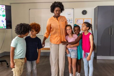 Teacher standing with children hugging and laughing in bright classroom promoting teamwork